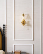Distant view of a lit Clérachic gold cherub wall light on a white panelled wall above a bedside table.