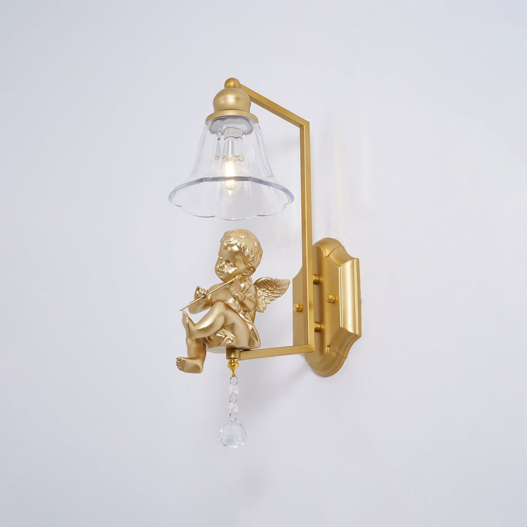Gold cherub wall light from Clérachic with a clear bell shade and a crystal drop, against a plain pale wall.
