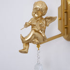 Close view of a gold cherub playing a violin, with a crystal ball drop below on this Clérachic wall light.