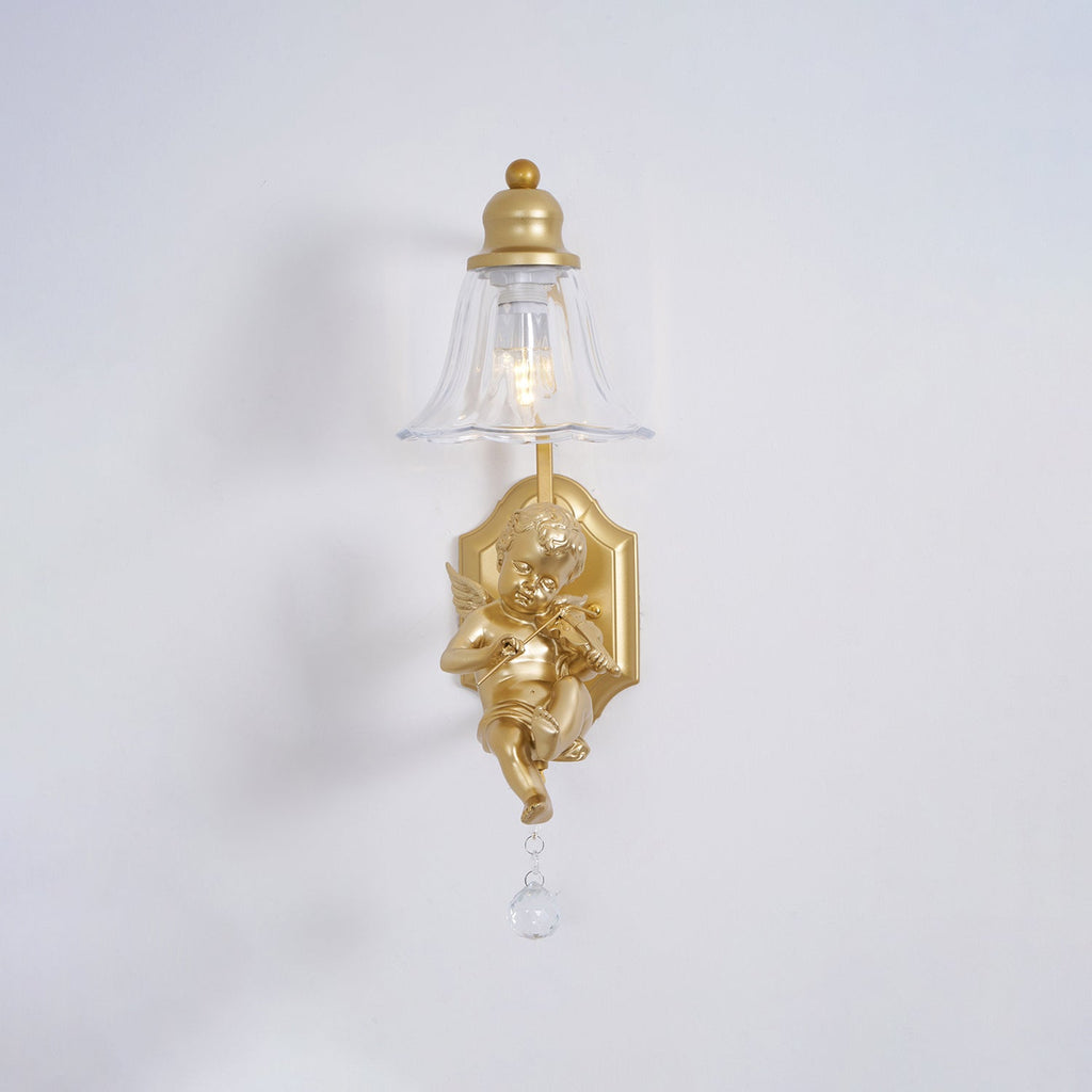 Front view of a Clérachic gold wall light, its clear bell shade above a cherub and a crystal drop on a pale grey wall.