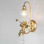 Side view of a lit Clérachic gold wall light with a trumpet-playing cherub, a curved arm and a round backplate.