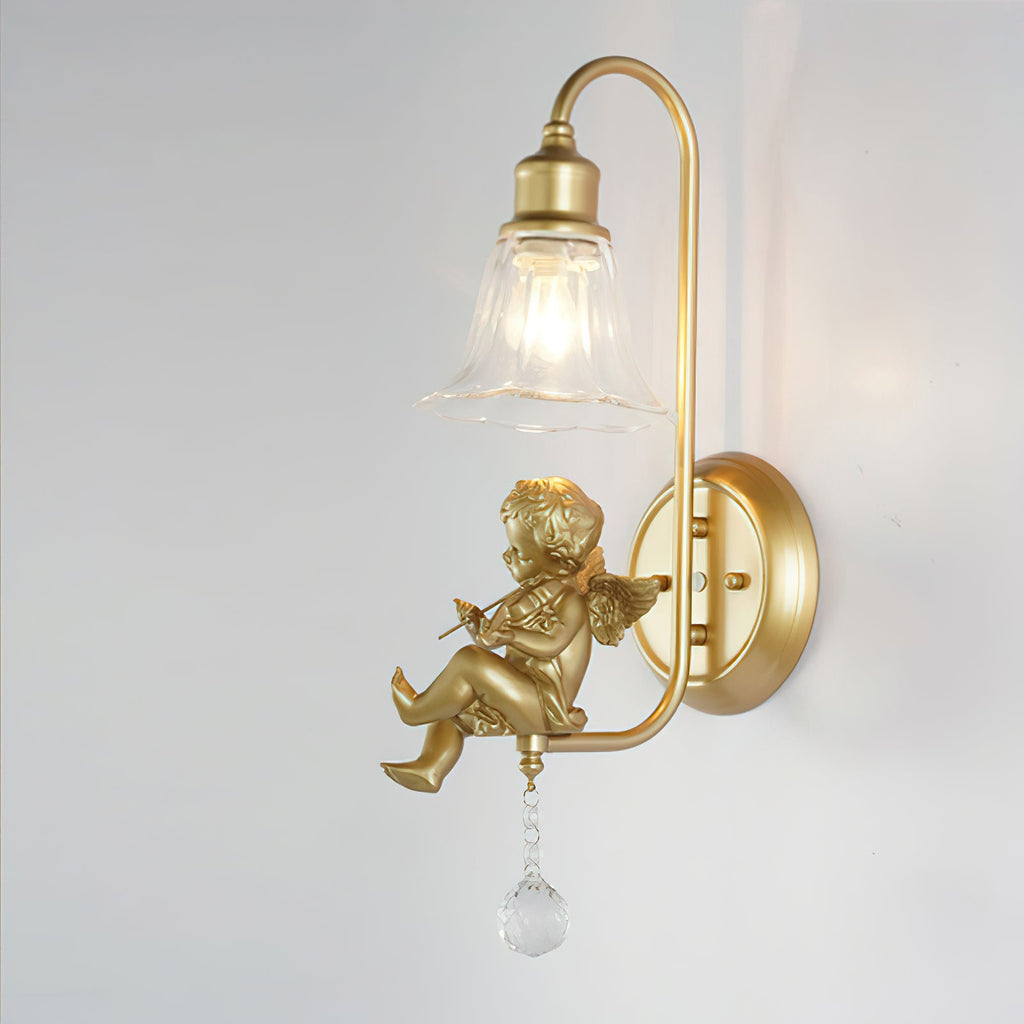 Side view of a lit Clérachic gold wall light with a cherub playing a violin, hung from a curved arm on a round backplate.
