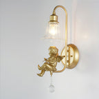 Side view of a lit Clérachic gold wall light with a cherub playing a violin, hung from a curved arm on a round backplate.