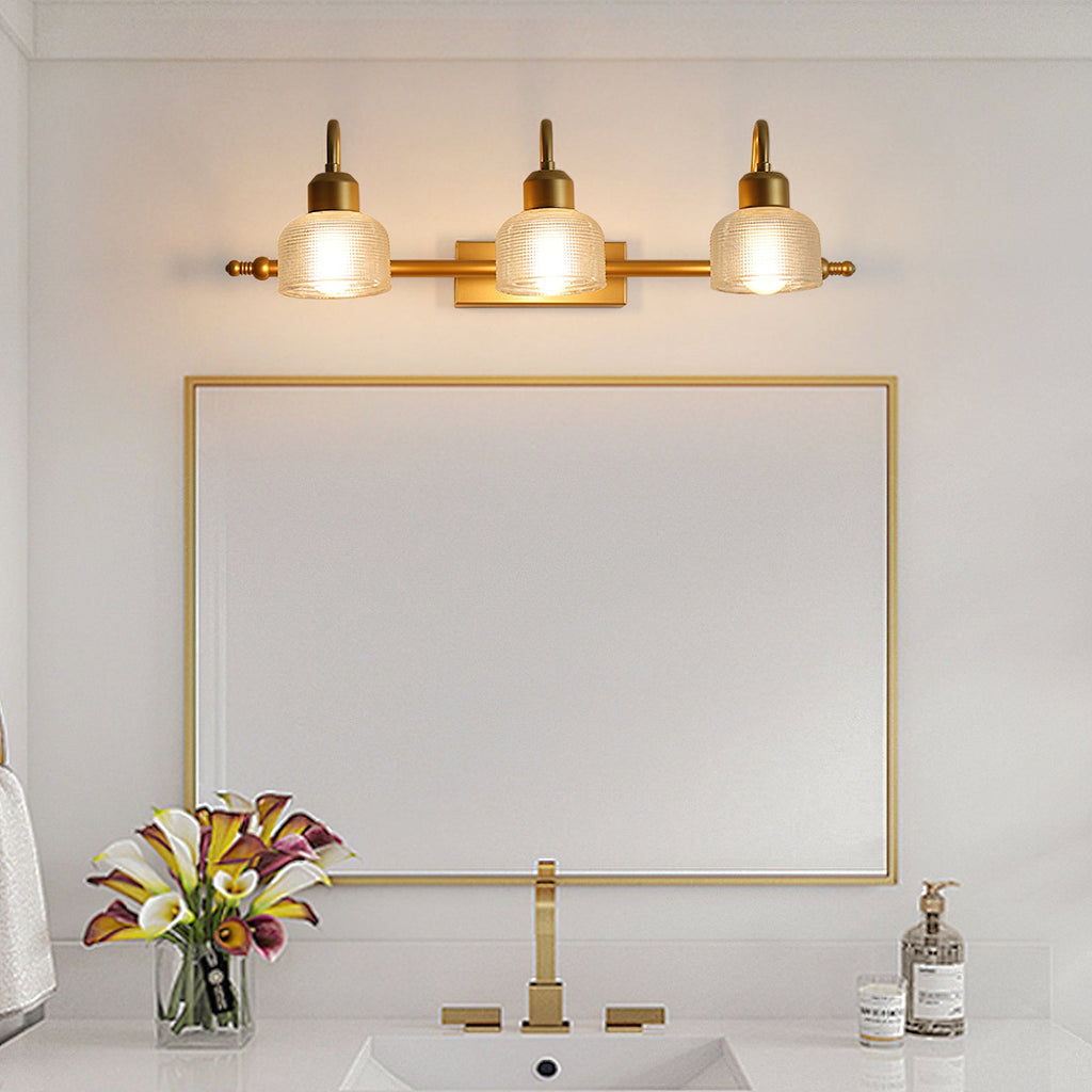 Three gold arms with warm-glowing ribbed shades sit above a rectangular gold-framed mirror and a gold tap on this Clérachic wall lamp.
