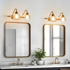 A pair of two-light Clérachic wall lamps above two rounded mirrors over a double vanity, with a potted plant between the basins.