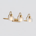 Three-light Clérachic wall lamp with clear ribbed glass shades glowing softly on a long gold bar, shown against a light grey backdrop.