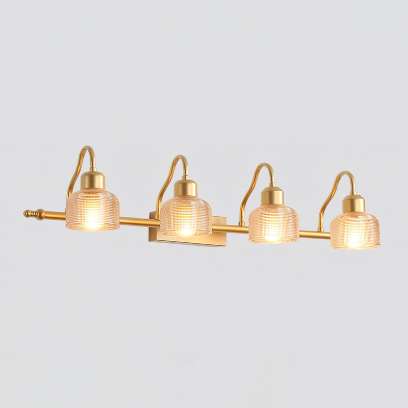 Four-light Clérachic wall lamp with warm amber ribbed glass shades lit along a slim gold bar, on a pale grey background.