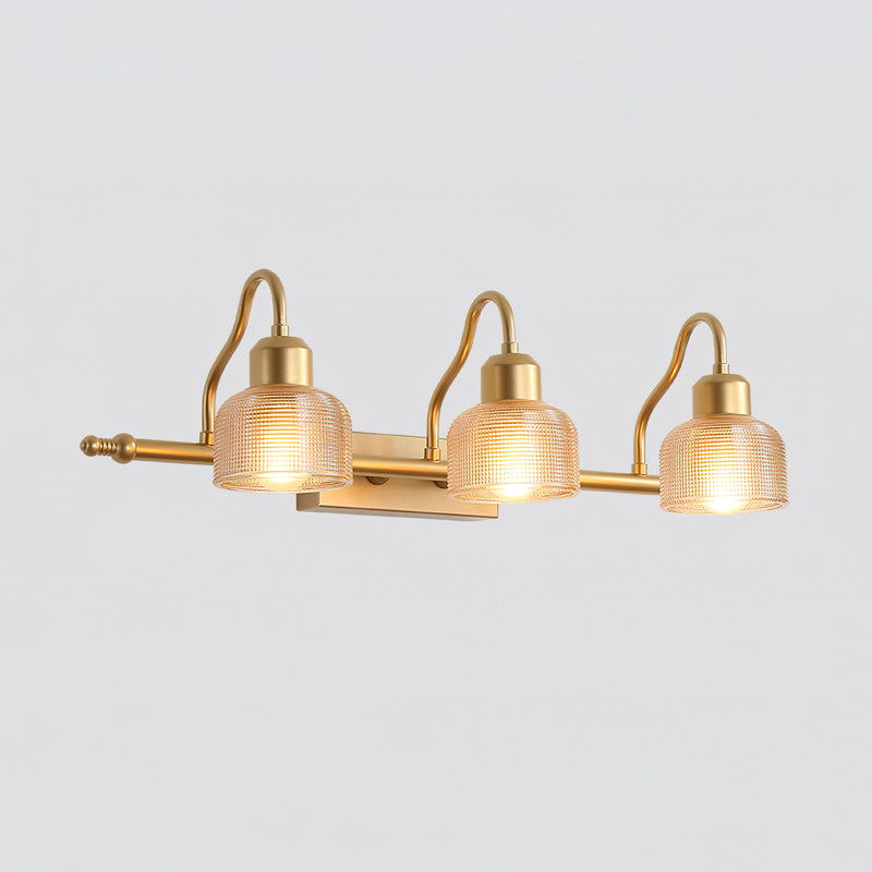 Three amber ribbed glass shades glow on the curved gold arms of this Clérachic wall lamp, shown against a pale grey backdrop.