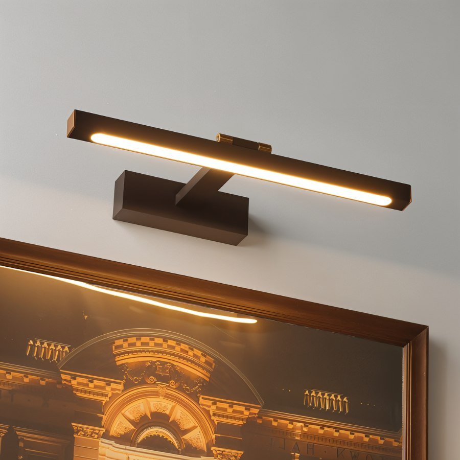 A Clérachic wall lamp in bronze-brown lights a framed architectural print of a golden-lit building from above.
