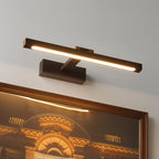 A Clérachic wall lamp in bronze-brown lights a framed architectural print of a golden-lit building from above.