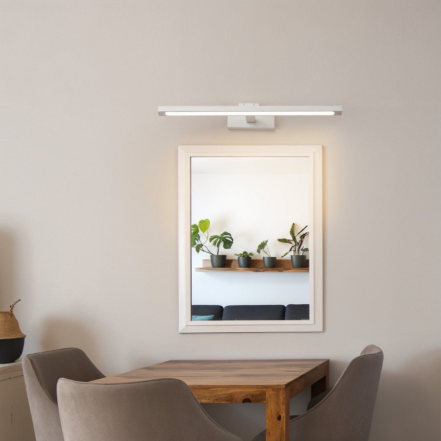 A Clérachic wall lamp in white lights a framed mirror above a dining table with potted plants.