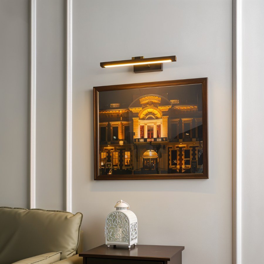 A Clérachic wall lamp in bronze-brown glows above a framed cityscape photograph, beside a small lantern on a side table.