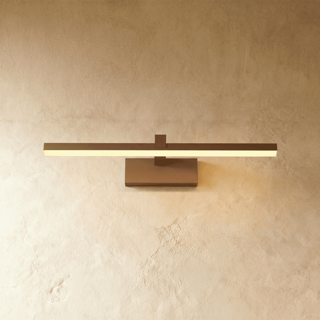 Clérachic bronze linear wall light with a slim horizontal bar and rectangular wall plate against a plaster wall.