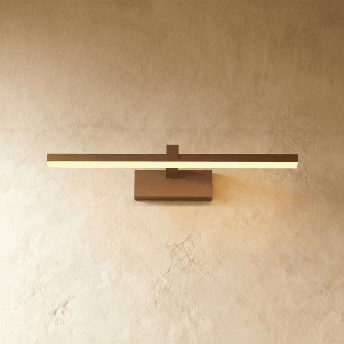 Clérachic bronze linear wall light with a slim horizontal bar and rectangular wall plate against a plaster wall.