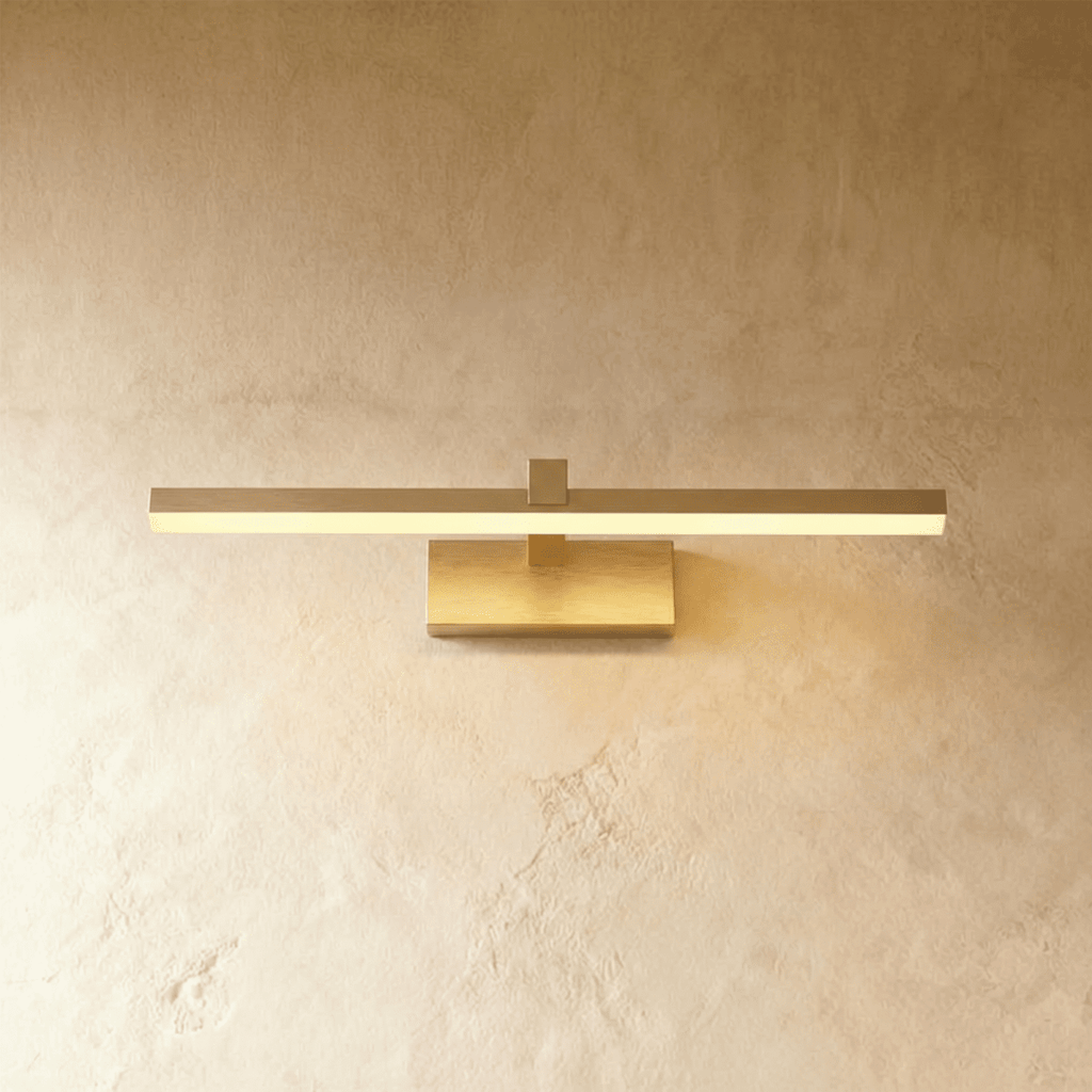 Clérachic brass linear wall light with a slim horizontal bar and rectangular wall plate glowing warm on plaster.