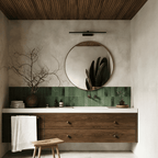 Clérachic black linear wall light mounted above a round mirror in a green-tiled bathroom with wood cabinetry.
