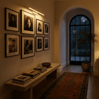 Clérachic white linear wall light glowing above a gallery wall of framed portraits in a hallway at dusk.
