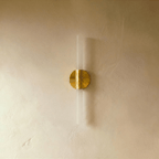 An angled studio view of the Clérachic Ena wall lamp's gold disc mount and frosted glass diffuser.