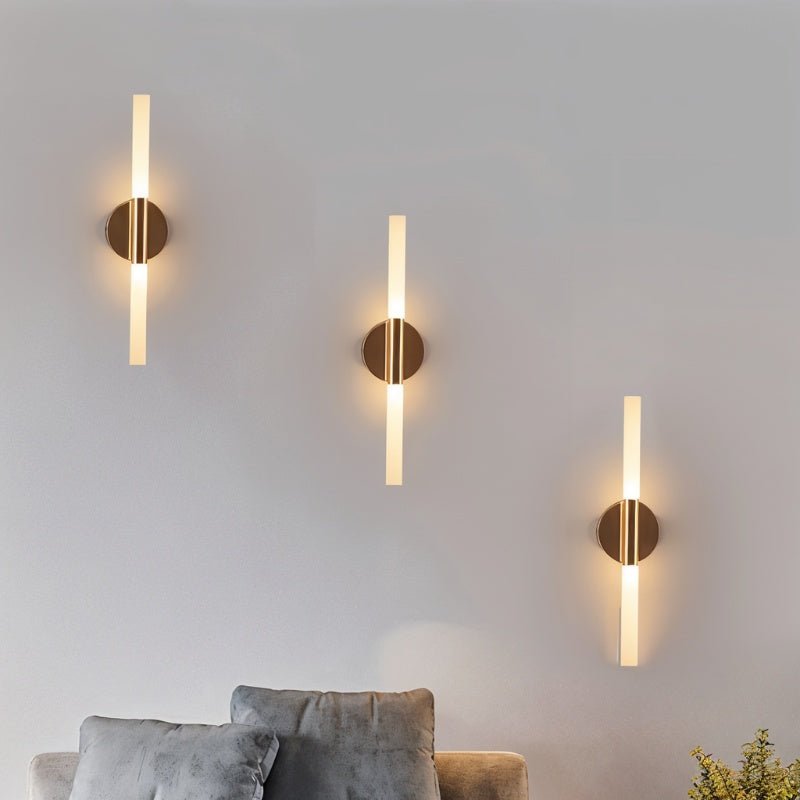 Three Clérachic Ena wall lamps in gold light a grey wall above a plush sofa in a living room.