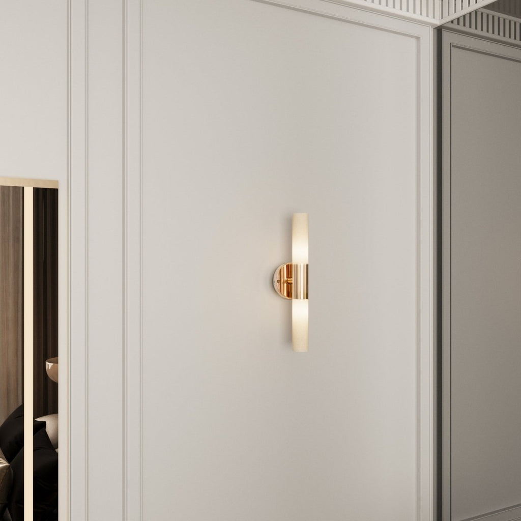 A Clérachic Ena wall lamp in gold glows softly on a panelled wall beside a mirrored wardrobe.