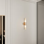 A Clérachic Ena wall lamp in gold glows softly on a panelled wall beside a mirrored wardrobe.