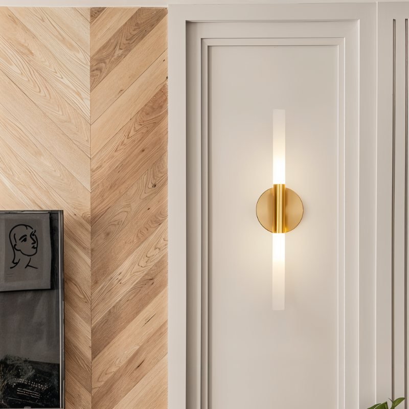 Close-up of the Clérachic Ena wall lamp in gold mounted on a white door beside herringbone wood panelling.
