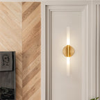Close-up of the Clérachic Ena wall lamp in gold mounted on a white door beside herringbone wood panelling.