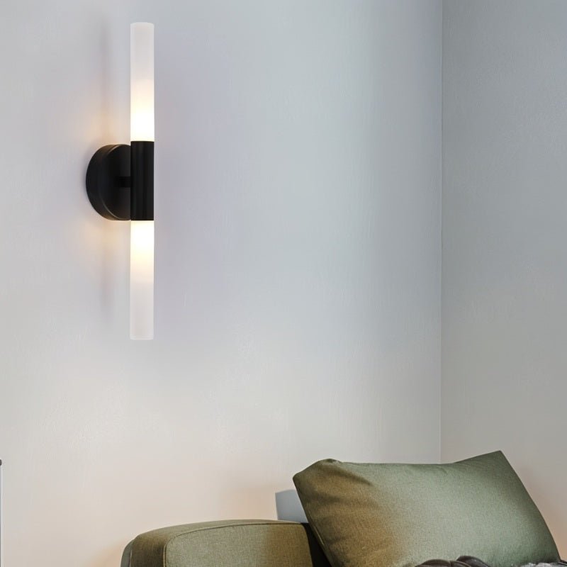 A Clérachic Ena wall lamp in black glows above a green upholstered armchair in a soft grey room.