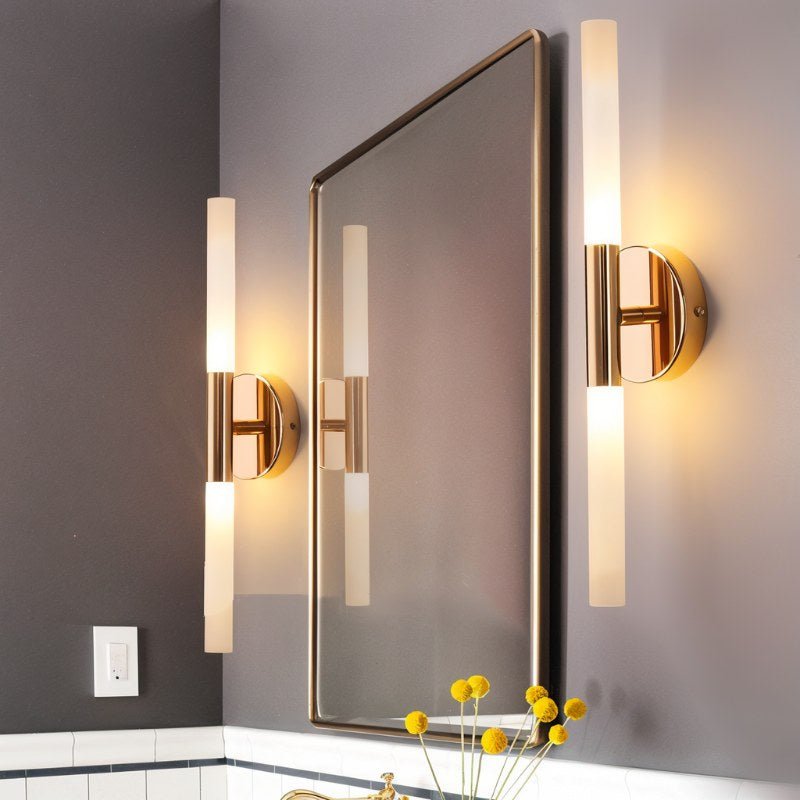Two Clérachic Ena wall lamps in gold flank a bathroom mirror above a marble-topped vanity.