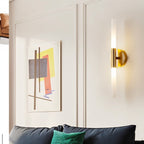 A Clérachic Ena wall lamp in gold lights a cream panelled wall above a dark blue leather sofa.