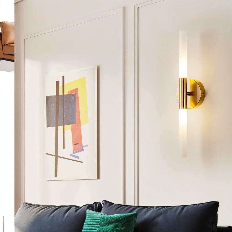 A Clérachic Ena wall lamp in gold lights a cream panelled wall above a dark blue leather sofa.