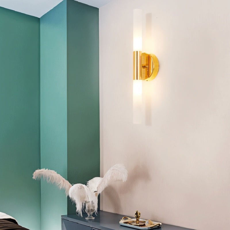 A Clérachic Ena wall lamp in gold lights a bedroom corner where teal walls meet a soft cream panel.