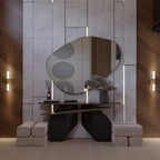 Two Clérachic Ena wall lamps in gold flank an organic mirror in a marble and wood-panelled entryway.