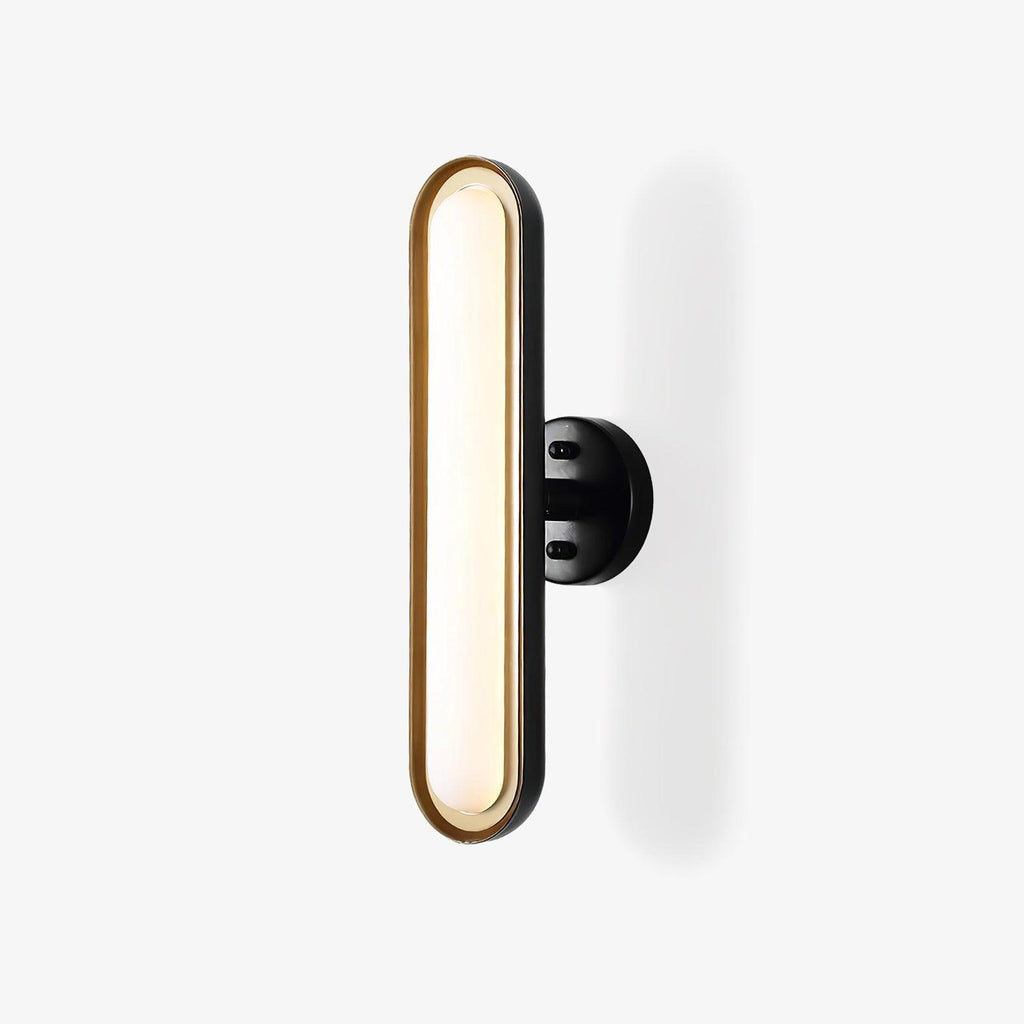 A Clérachic capsule wall light on a plain white backdrop: a frosted white oval lens in a gold rim, on a round black wall plate.