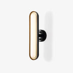 A Clérachic capsule wall light on a plain white backdrop: a frosted white oval lens in a gold rim, on a round black wall plate.