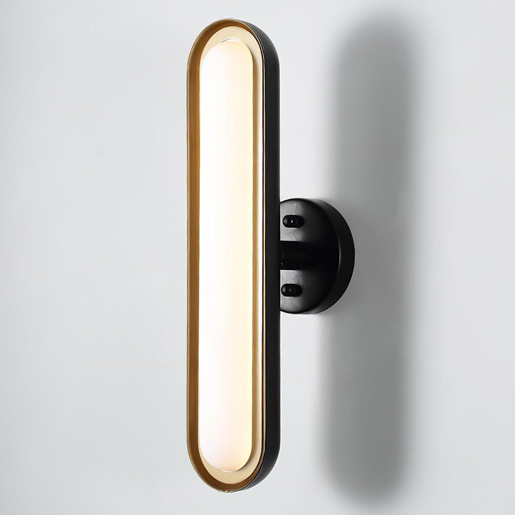 Close view of a tall frosted white capsule lens in a gold rim on a round black wall plate, against a pale wall, from Clérachic.