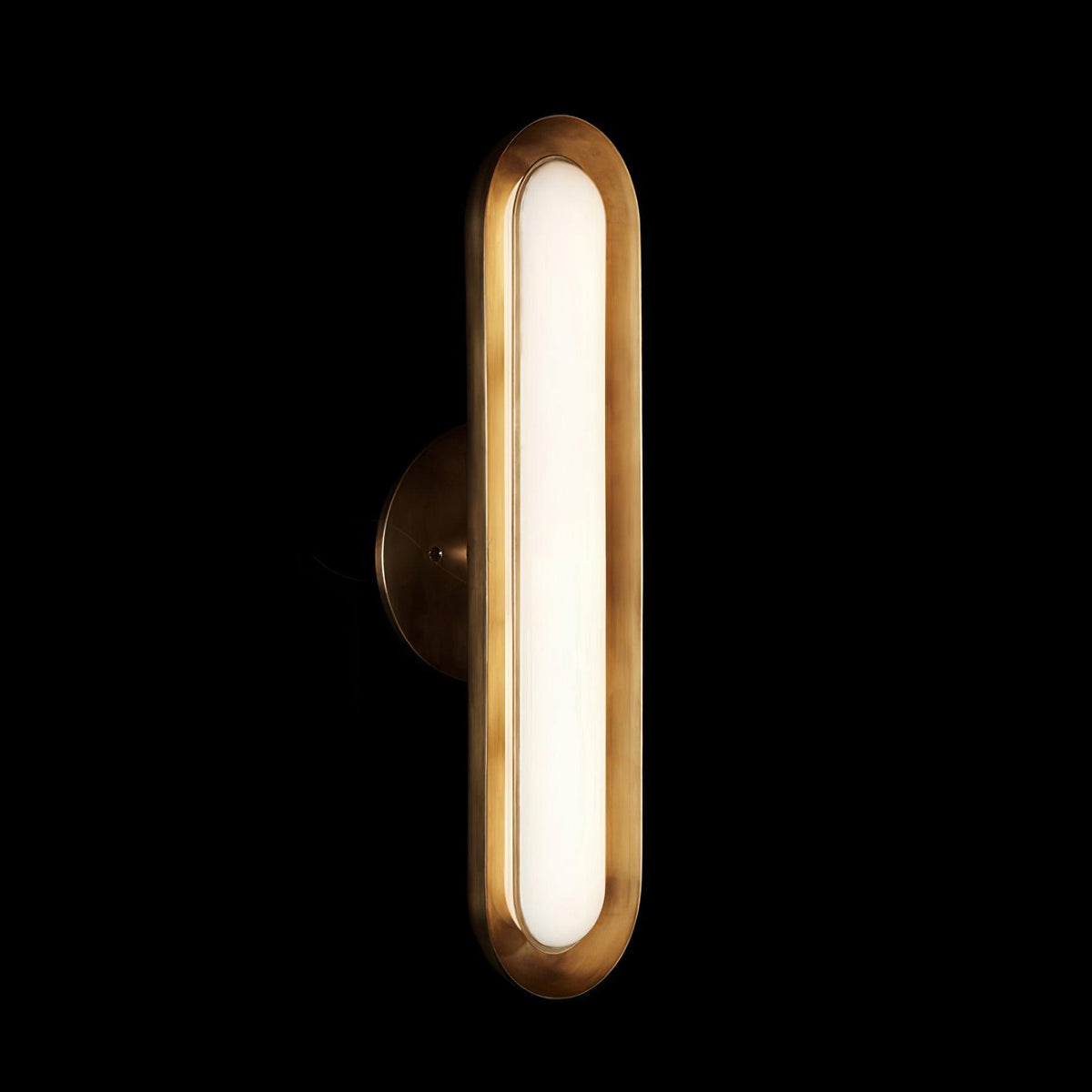 Lit against a black backdrop, this Clérachic capsule wall light shows a brushed gold rim and a glowing frosted white lens.