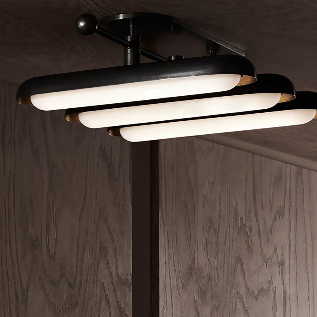 Seen from above and to the side, three stacked capsule lights step down from a black frame with gold edges, from Clérachic.