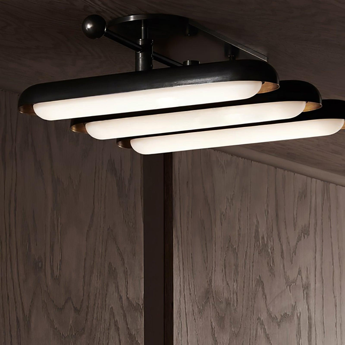 Seen from above and to the side, three stacked capsule lights step down from a black frame with gold edges, from Clérachic.