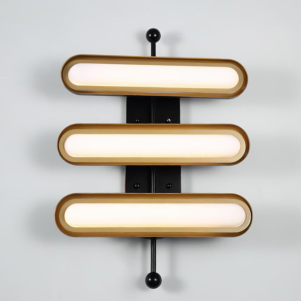 Three frosted capsule lenses of different lengths in gold rims on a black bar with round black ends, on a pale grey wall, from Clérachic.