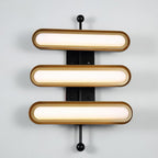 Three frosted capsule lenses of different lengths in gold rims on a black bar with round black ends, on a pale grey wall, from Clérachic.