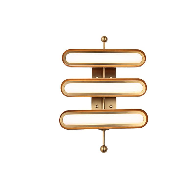 A three-capsule wall light with frosted lenses, a gold backplate and round gold ends, on a white backdrop, from Clérachic.