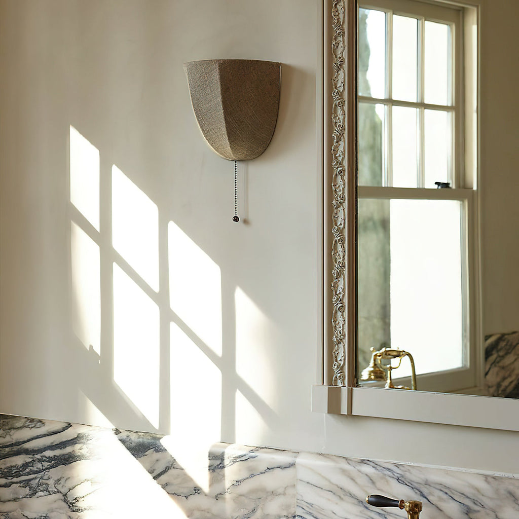 Unlit Clérachic linen wall sconce on a sunlit wall beside a framed window and a marble vanity with brass taps.