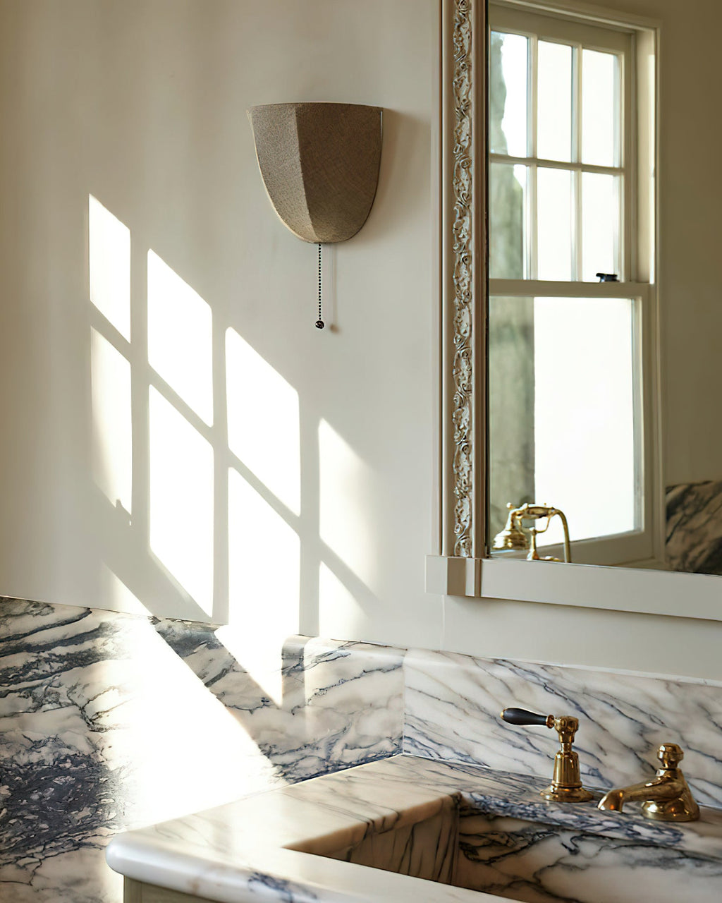Clérachic linen wall sconce on a wall with window light and shadows, above a marble basin with brass taps.