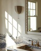 Clérachic linen wall sconce on a wall with window light and shadows, above a marble basin with brass taps.