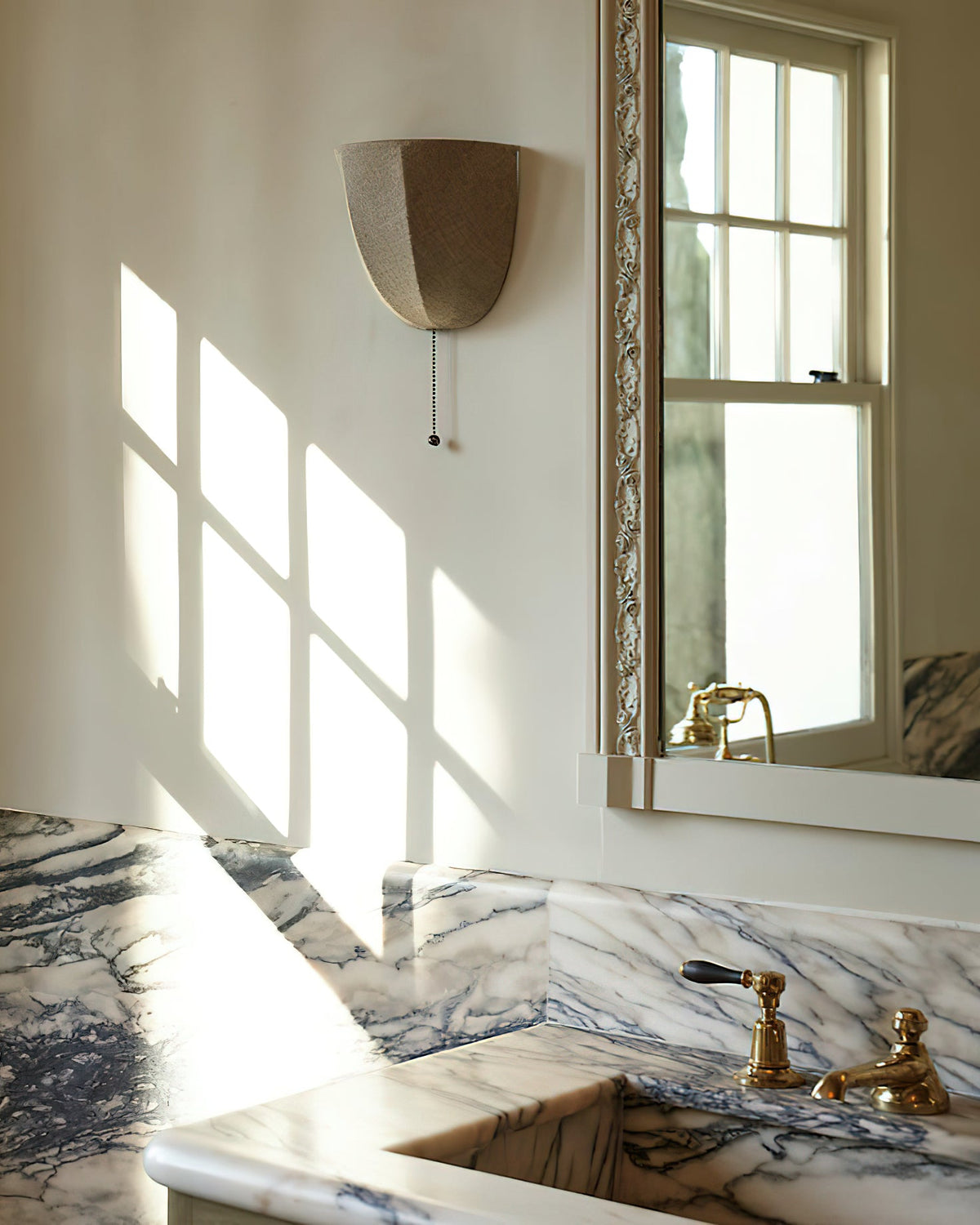 Clérachic linen wall sconce on a wall with window light and shadows, above a marble basin with brass taps.