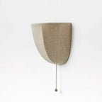 Side view of an unlit Clérachic linen wall sconce, showing its flat back and curved shade on a white wall.