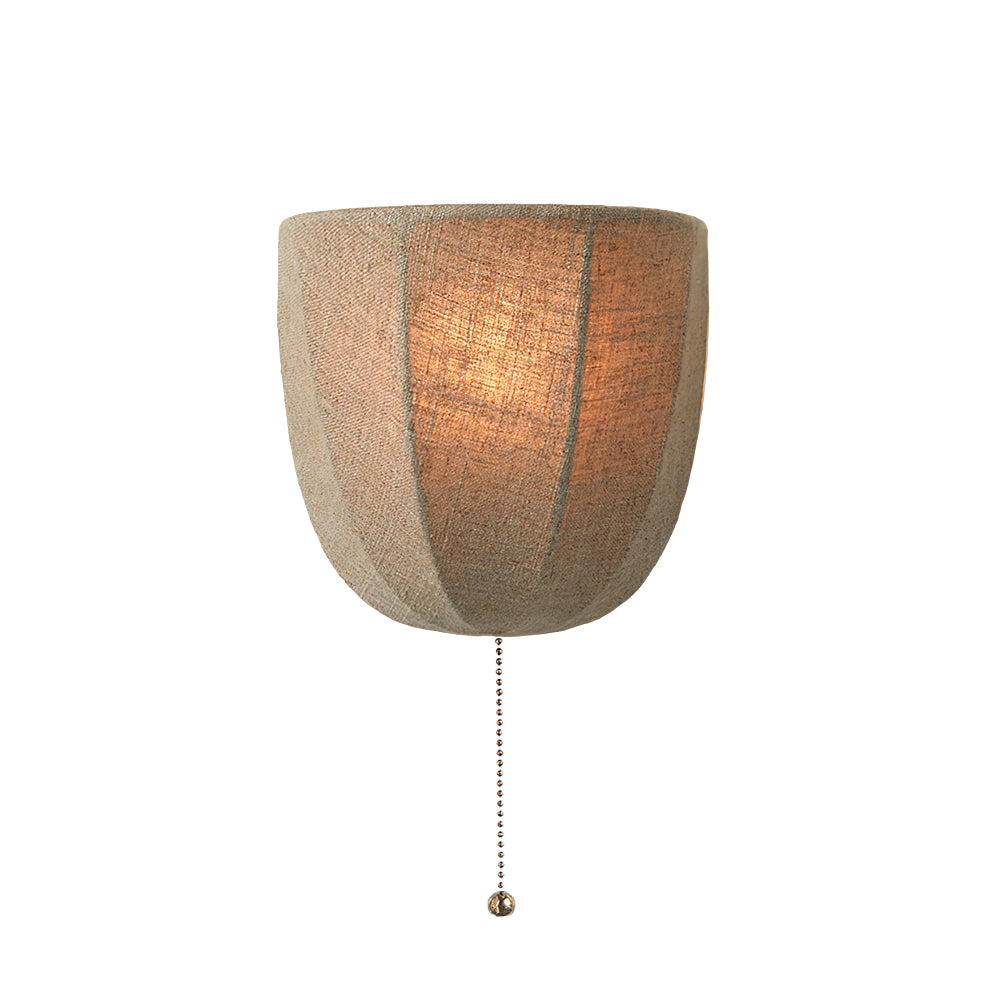 Lit Clérachic linen wall sconce on a white backdrop, its shade glowing warm with a beaded pull chain hanging below.