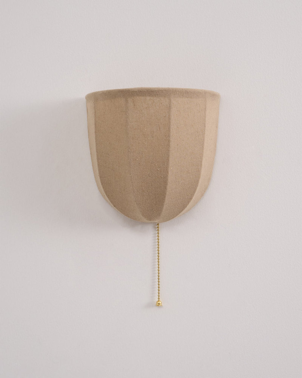 Unlit Clérachic linen wall sconce on a pale wall, with soft vertical seams and a gold-toned pull chain.