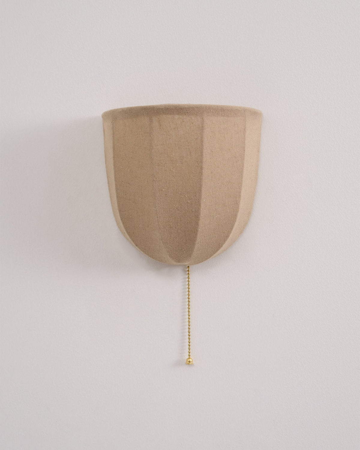 Unlit Clérachic linen wall sconce on a pale wall, with soft vertical seams and a gold-toned pull chain.
